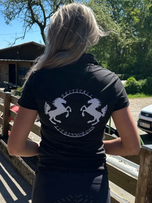 Person mit schwarzem Shirt mit zwei weißen springenden Pferden und Text Reitstall Siebenmorgen.